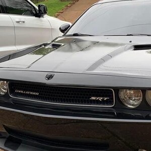 以下が含まれることがあります： 黒いグリルと銀色の SRT の文字が書かれた黒い Dodge Challenger SRT。車は車道に駐車されています。