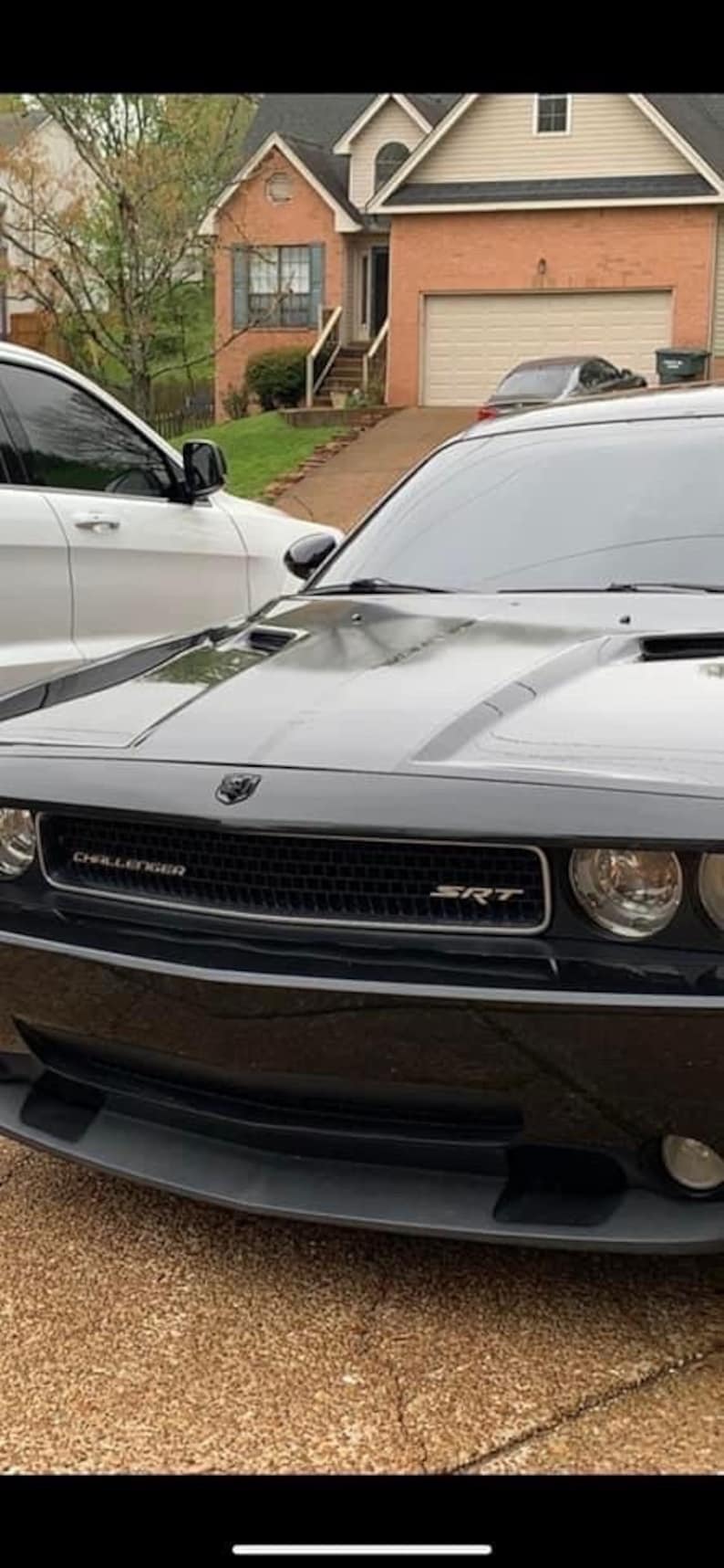 以下が含まれることがあります： 黒いグリルと銀色の SRT の文字が書かれた黒い Dodge Challenger SRT。車は車道に駐車されています。