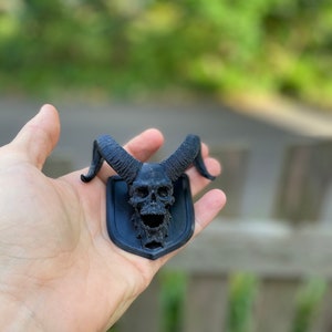 以下が含まれることがあります： 黒い3Dプリントされた頭蓋骨に角が取り付けられた黒いプレート。頭蓋骨は詳細なデザインで、装飾品です