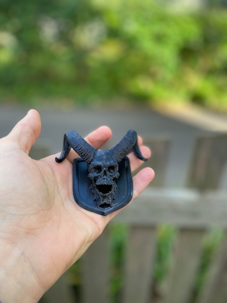 以下が含まれることがあります： 黒い3Dプリントされた頭蓋骨に角が取り付けられた黒いプレート。頭蓋骨は詳細なデザインで、装飾品です