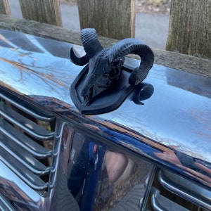 Puede incluir: Un cráneo de carnero negro impreso en 3D con cuernos, montado sobre una base negra. El cráneo es detallado y realista, con dientes y estructura ósea visibles.