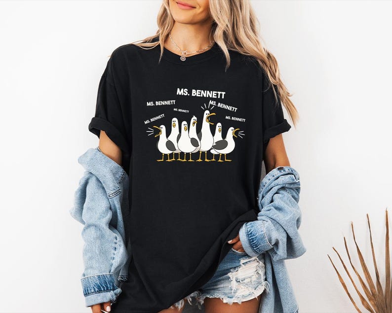 A woman wearing a black t-shirt with a graphic of seagulls and text that says "MS. BENNETT" along with the names "MS. BENNETT" and "MS. BENNETT" repeated around the graphic.