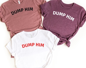 May include: Three t-shirts with the text "DUMP HIM" printed on them. The shirts are in different colors: pink, purple, and white. The text on the white shirt is red.
