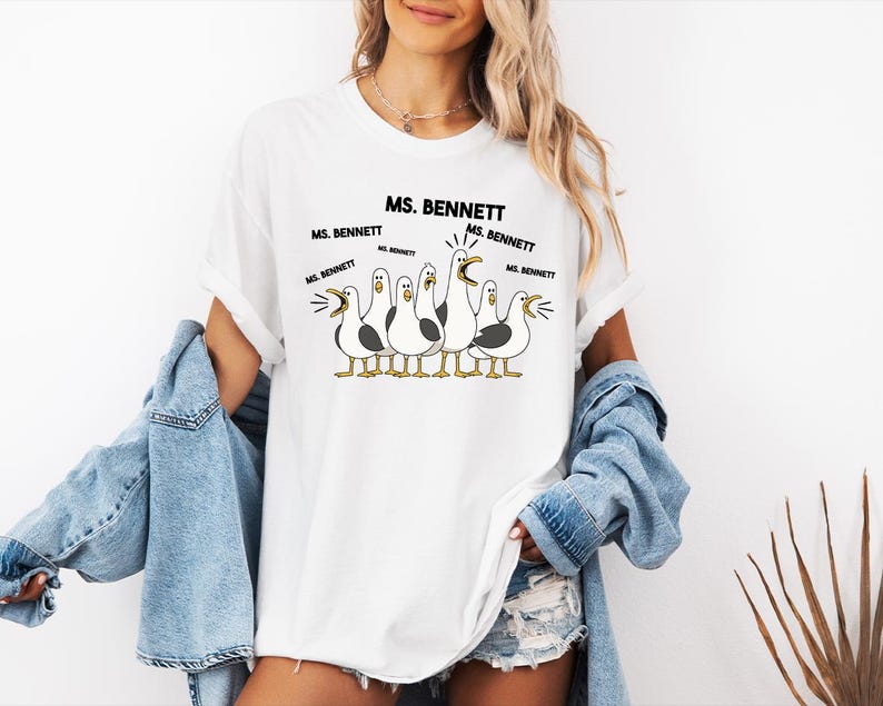 A woman wearing a white t-shirt with a graphic of five seagulls and text that says "MS. BENNETT MS. BENNETT".