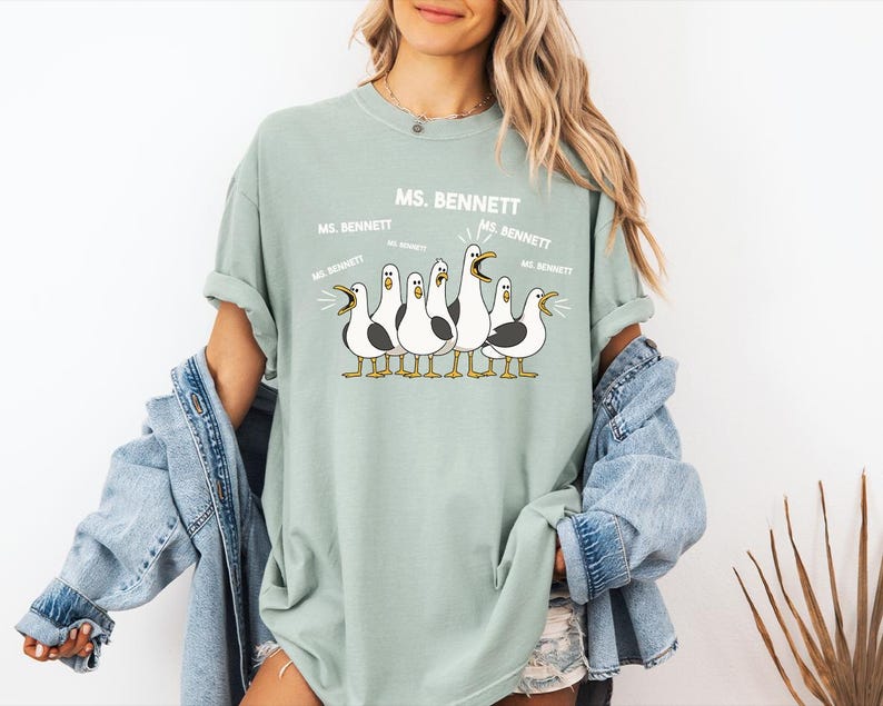 A woman wearing a green t-shirt with a graphic of a group of seagulls and text that says "MS. BENNETT MS. BENNETT".