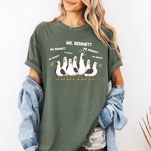 A woman wearing a green t-shirt with a graphic of seagulls and text that says "MS. BENNETT" and "MS. BENNETT" repeated several times.