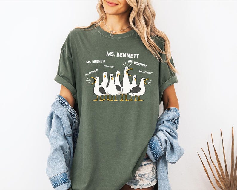 A woman wearing a green t-shirt with a graphic of seagulls and text that says "MS. BENNETT" and "MS. BENNETT" repeated several times.