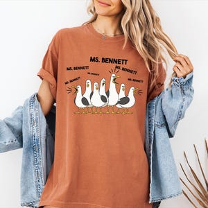 A woman wearing a t-shirt with a cartoon of seagulls and text that says "MS. BENNETT MS. BENNETT".