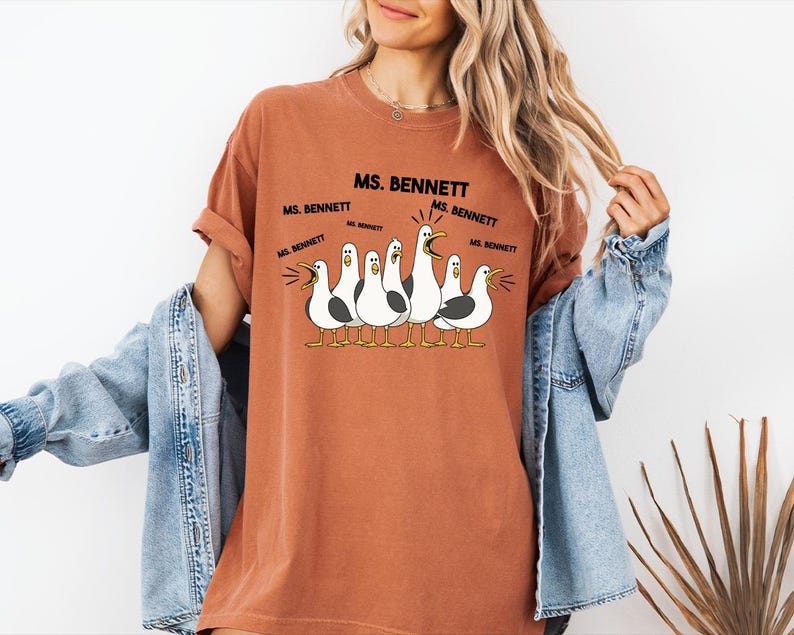 A woman wearing a t-shirt with a cartoon of seagulls and text that says "MS. BENNETT MS. BENNETT".