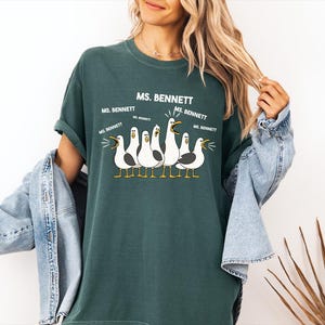 A woman wearing a green t-shirt with a graphic of seagulls and text that says "MS. BENNETT" and "MS. BENNETT" repeated five times.