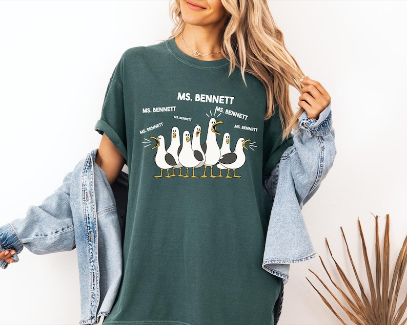 A woman wearing a green t-shirt with a graphic of seagulls and text that says "MS. BENNETT" and "MS. BENNETT" repeated five times.