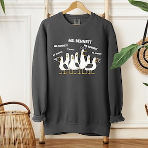 A gray sweatshirt with a graphic design of a group of seagulls and text that says "MS. BENNETT" and "MS. BENNETT" repeated several times.