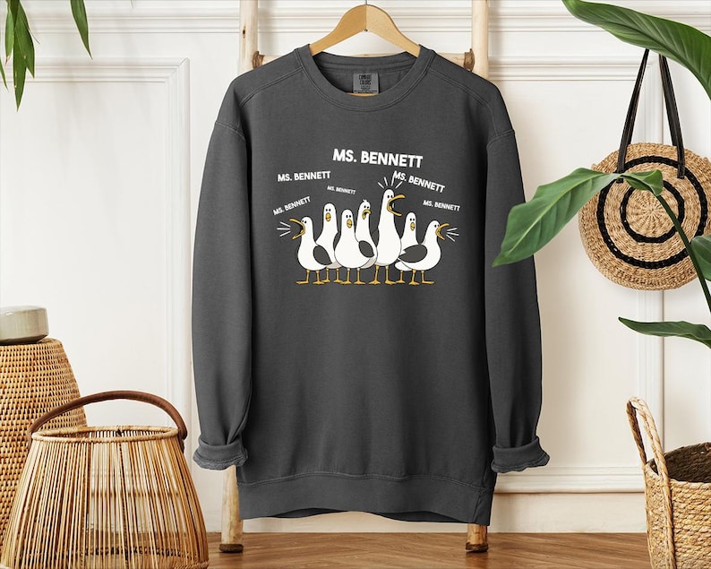 A gray sweatshirt with a graphic design of a group of seagulls and text that says "MS. BENNETT" and "MS. BENNETT" repeated several times.