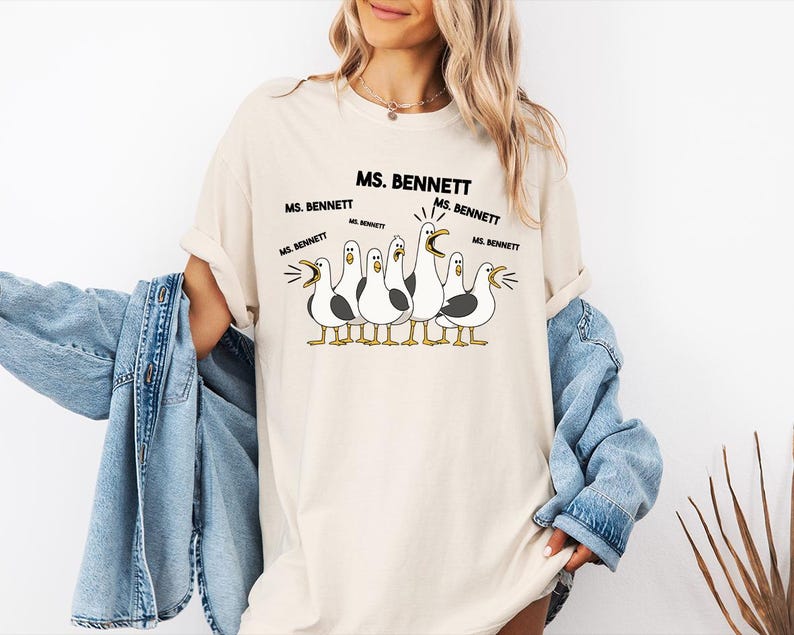 A woman wearing a white t-shirt with a graphic of a group of seagulls and text that says "MS. BENNETT MS. BENNETT".