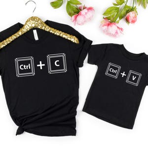 May include: Two black t-shirts with white text. The larger shirt says "Ctrl + C" and the smaller shirt says "Ctrl + V".