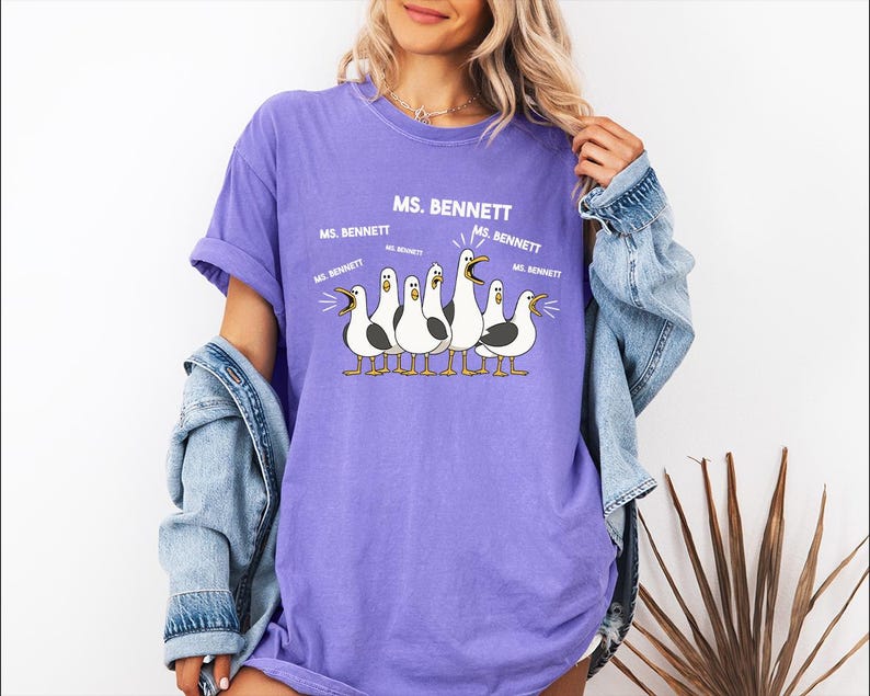 A woman wearing a purple t-shirt with a graphic of a group of seagulls and text that says "MS. BENNETT".