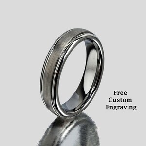 May include: A silver tungsten carbide ring with a brushed finish and a beveled edge. Free custom engraving is offered.