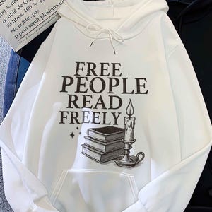 May include: A white hoodie with a front pocket and the text "FREE PEOPLE READ FREELY" in black. The graphic includes a stack of books and a candle. A black hoodie is next to it.
