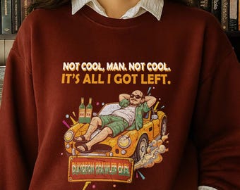 May include: A maroon sweatshirt with the text "NOT COOL, MAN. NOT COOL. IT'S ALL I GOT LEFT." features a cartoon of a man relaxing in a yellow car. The graphic includes two beer bottles and the words "DUNGEON CRAWLER CAR".