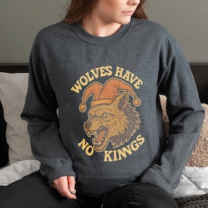 May include: Dark gray sweatshirt featuring a wolf wearing a jester's hat. The graphic includes the text "WOLVES HAVE NO KINGS" in a circular design. The wolf is depicted with an open mouth and detailed fur.