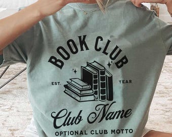 May include: A pale green t-shirt featuring the text "BOOK CLUB" above a graphic of books. Below the graphic are the words "Club Name" and "Optional Club Motto". The shirt has short sleeves.
