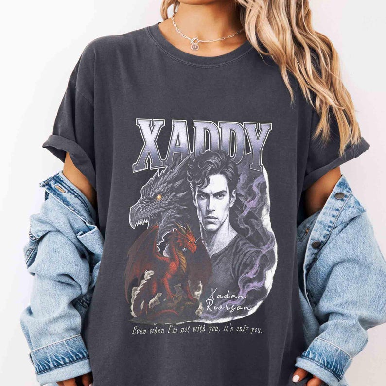 Puede incluir: Camiseta gris oscuro con la palabra "XADDY" sobre un gr&aacute;fico de un hombre y dos dragones. Tambi&eacute;n se ve el texto "Kaden Riordan" y "Even when I'm not with you, it's only you".