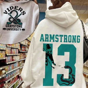 May include: White hoodie with the text "VIPERS" and "GRAYSTONE UNIVERSITY" in black and teal. The back of the hoodie features the name "ARMSTRONG" and the number "13" in teal, along with a snake graphic.
