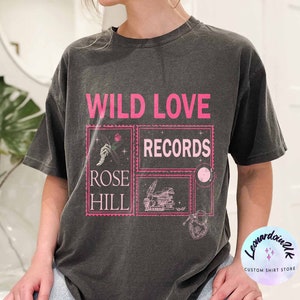 May include: A black t-shirt with a pink graphic design that says "Wild Love Records" with a smaller graphic that says "Rose Hill".