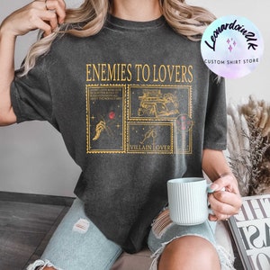 Puede incluir: Una camiseta negra con un estampado gr&aacute;fico de tem&aacute;tica de club de lectura. El texto de la camiseta dice "Enemies to Lovers" y "Villain Lover".
