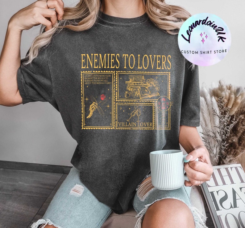 Puede incluir: Una camiseta negra con un estampado gr&aacute;fico de tem&aacute;tica de club de lectura. El texto de la camiseta dice "Enemies to Lovers" y "Villain Lover".