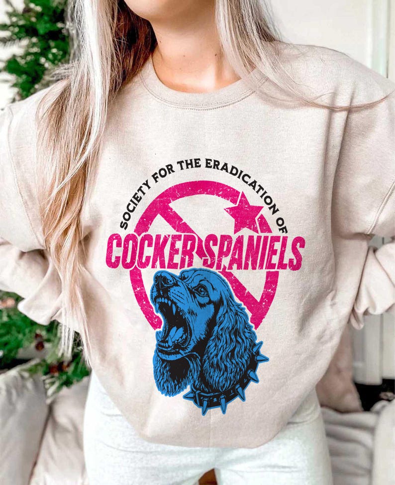 May include: Beige sweatshirt with a graphic that reads "SOCIETY FOR THE ERADICATION OF COCKER SPANIELS." The graphic features a blue Cocker Spaniel with an open mouth inside a pink circle with a star.