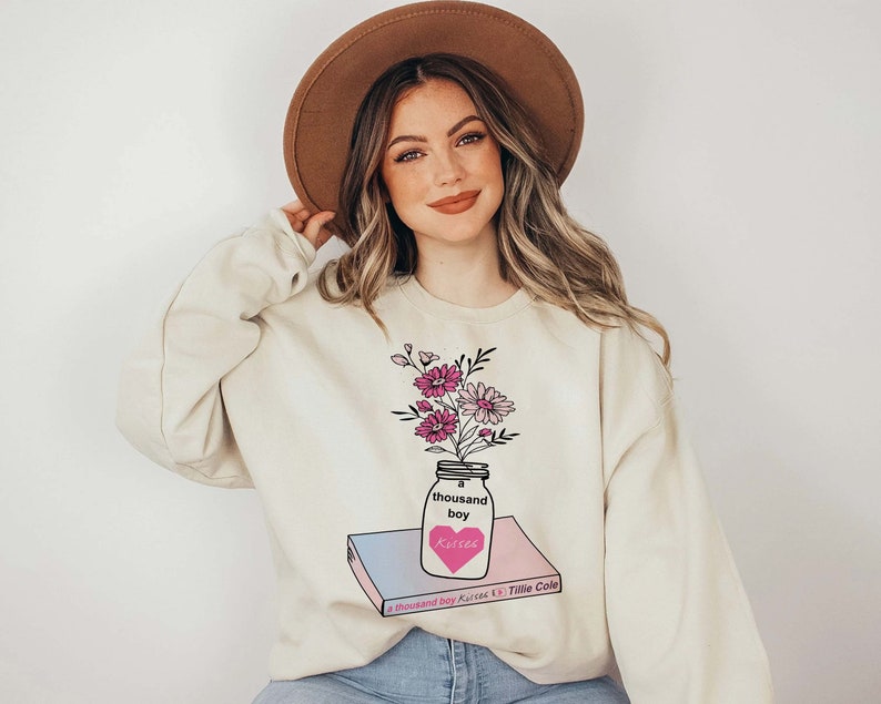 May include: A cream colored sweatshirt with a graphic of a mason jar filled with pink flowers and the text "a thousand boy kisses" and "Tillie Cole".
