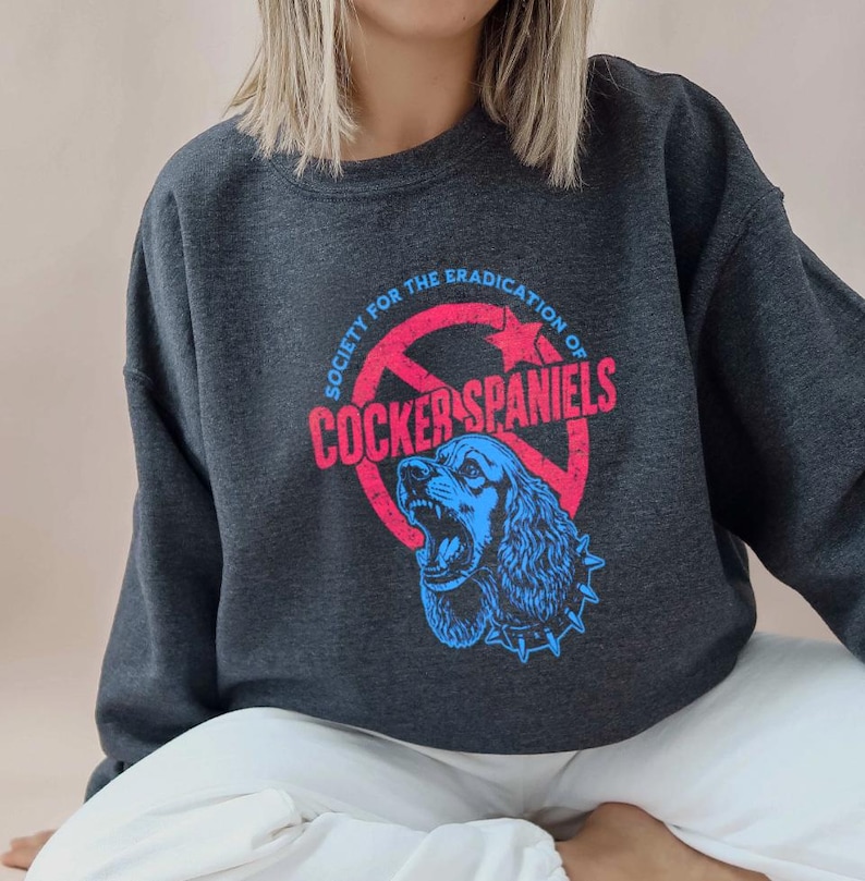 May include: Dark gray sweatshirt with a graphic featuring a blue Cocker Spaniel inside a red circle with the text "SOCIETY FOR THE ERADICATION OF COCKER SPANIELS" in red and blue.