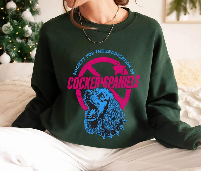 May include: Dark green sweatshirt with a graphic that reads "Society for the Eradication of Cocker Spaniels." The graphic features a blue Cocker Spaniel with an open mouth inside a pink circle with a red slash through it.