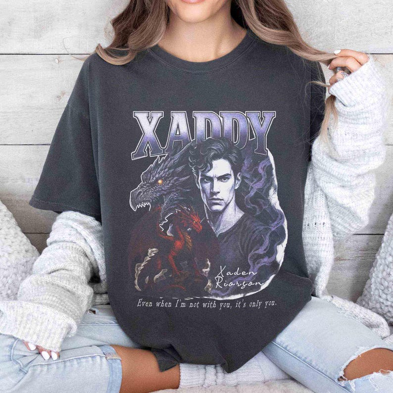 Puede incluir: Camiseta gris oscuro con un dise&ntilde;o gr&aacute;fico. El dise&ntilde;o presenta la palabra "XADDY" en morado y blanco, un drag&oacute;n, un retrato de hombre y el texto "Kaden Riordan" y "Even when I'm not with you, it's only you."