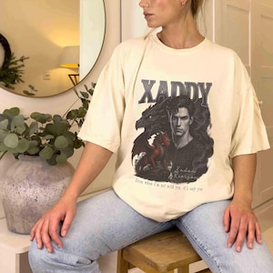 Puede incluir: Camiseta color crema con la palabra "XADDY" sobre un gr&aacute;fico de un hombre y un drag&oacute;n en negro y rojo. El texto "Even when I'm not with you, it's only you." est&aacute; debajo. La camiseta la lleva una persona.