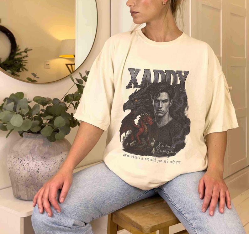 Puede incluir: Camiseta color crema con la palabra "XADDY" sobre un gr&aacute;fico de un hombre y un drag&oacute;n en negro y rojo. El texto "Even when I'm not with you, it's only you." est&aacute; debajo. La camiseta la lleva una persona.