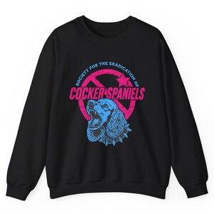 May include: Black sweatshirt with a graphic featuring a blue Cocker Spaniel with an open mouth and a spiked collar. The design includes the text "SOCIETY FOR THE ERADICATION OF COCKER SPANIELS" in pink and blue.