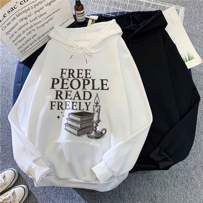 May include: A white hoodie with a front pocket and the text "FREE PEOPLE READ FREELY" in black. The graphic includes a stack of books and a candle. A black hoodie is next to it.