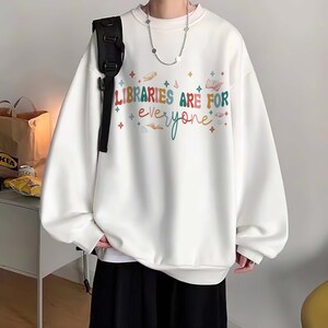 May include: White sweatshirt with a colorful graphic that says "Libraries are for everyone" with stars and books.