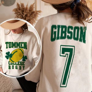May include: Cream-colored sweatshirt with green text and graphics. The front features the words "TOMMEN COLLEGE RUGBY" with a yellow football and shamrocks. The back displays "GIBSON" and the number "7" in green.