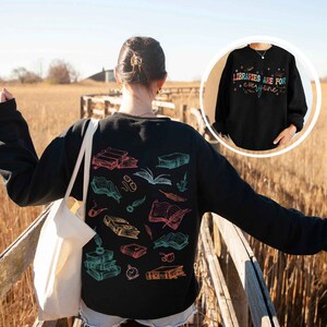 May include: Black sweatshirt with a colorful graphic of books and feathers. The text "LIBRARIES ARE FOR EVERYONE" is printed on a black sweatshirt in the background.