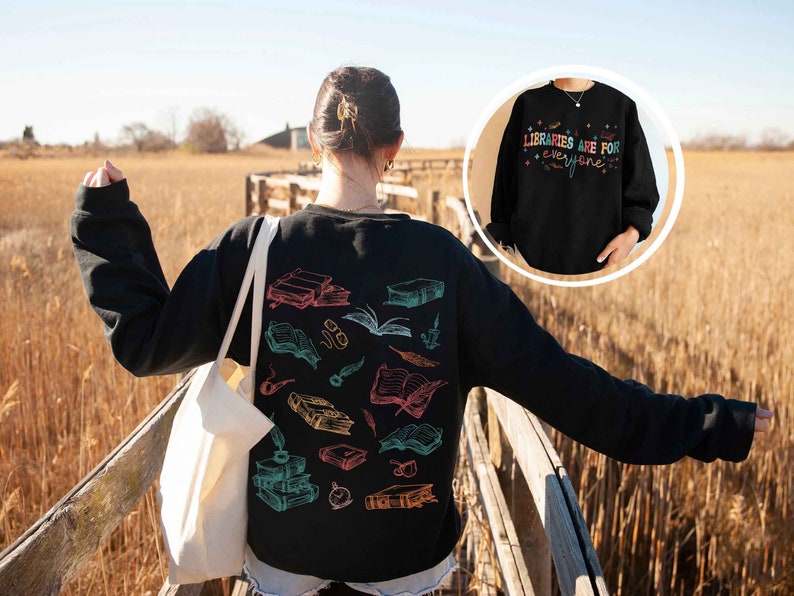 May include: Black sweatshirt with a colorful graphic of books and feathers. The text "LIBRARIES ARE FOR EVERYONE" is printed on a black sweatshirt in the background.