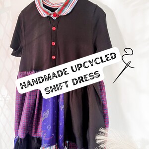 Puede incluir: Un vestido negro de corte recto con ribete de cuadros rojo, blanco y azul y un panel de tela con estampado azul y blanco. El vestido está hecho a mano y es reciclado. El texto "Handmade Upcycled Shift Dress" está escrito en una etiqueta blanca.