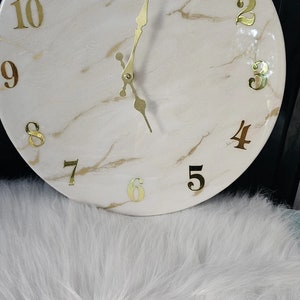 May include: A white clock with gold numbers and hands. The clock face has a marble-like design.