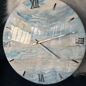 Puede incluir: Un reloj redondo con un dise&ntilde;o de m&aacute;rmol azul y blanco. La esfera del reloj tiene n&uacute;meros romanos y manecillas plateadas.