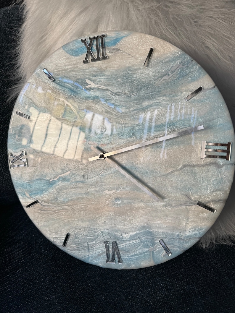 Puede incluir: Un reloj redondo con un dise&ntilde;o de m&aacute;rmol azul y blanco. La esfera del reloj tiene n&uacute;meros romanos y manecillas plateadas.