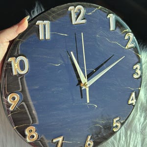 May include: A black and gold clock with a marble effect. The clock face has white Roman numerals and gold hands.