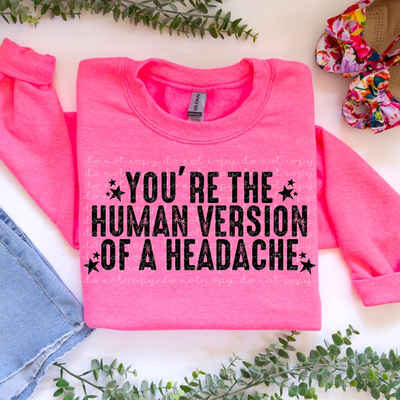 May include: A pink sweatshirt with the text "YOU'RE THE HUMAN VERSION OF A HEADACHE" in black with stars on either side of the text.