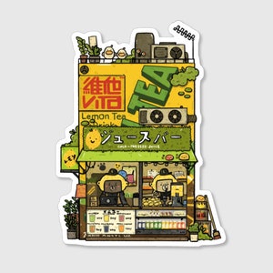 May include: A sticker featuring an illustrated juice bar with the text "TEA" and Japanese characters. The shop has a yellow exterior with green accents, and the words "Lemon Tea Drink" are visible. Two bear-like figures are behind the counter.